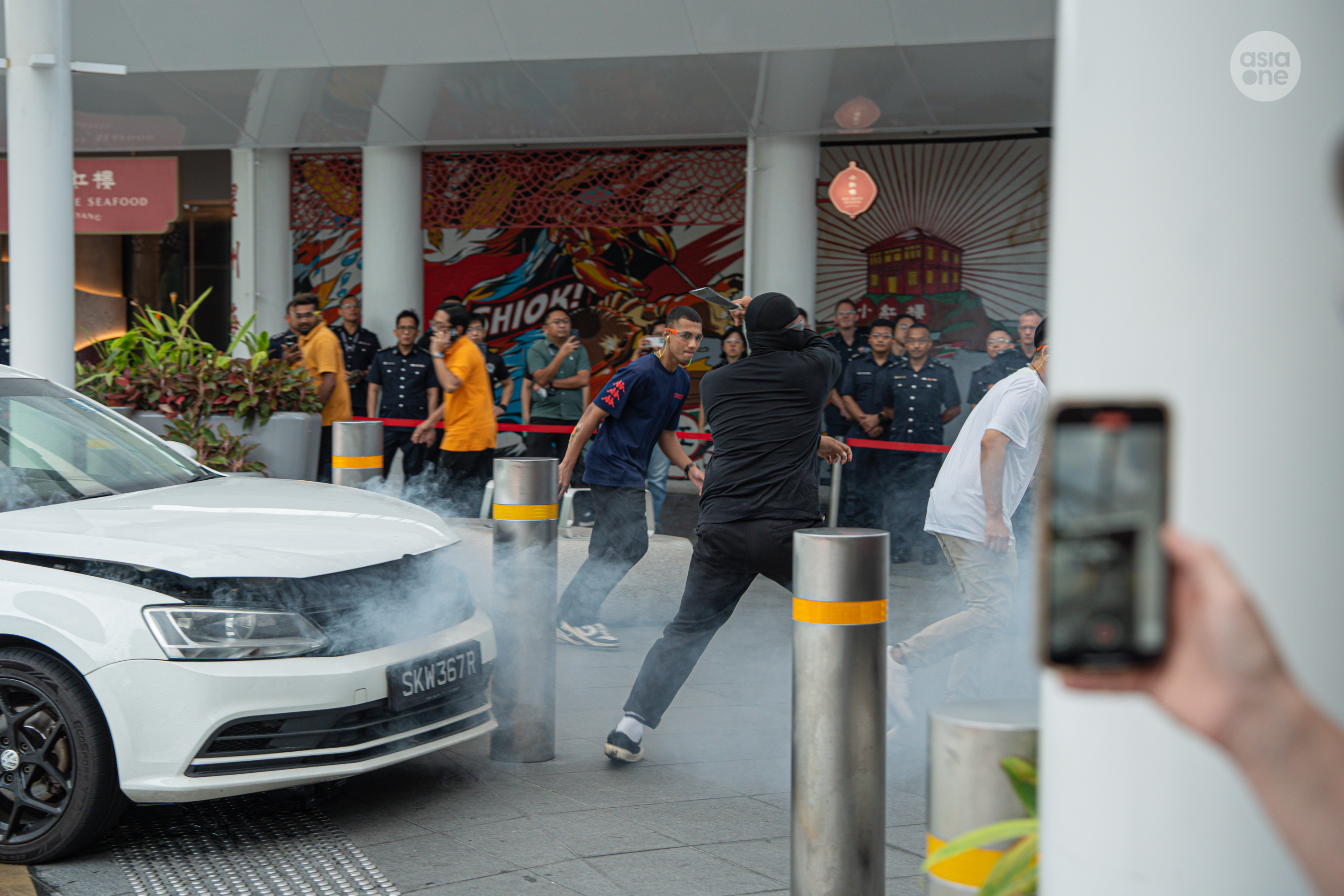 The driver of the white car crashes into a bollard and starts attacking passers-by with a machete.