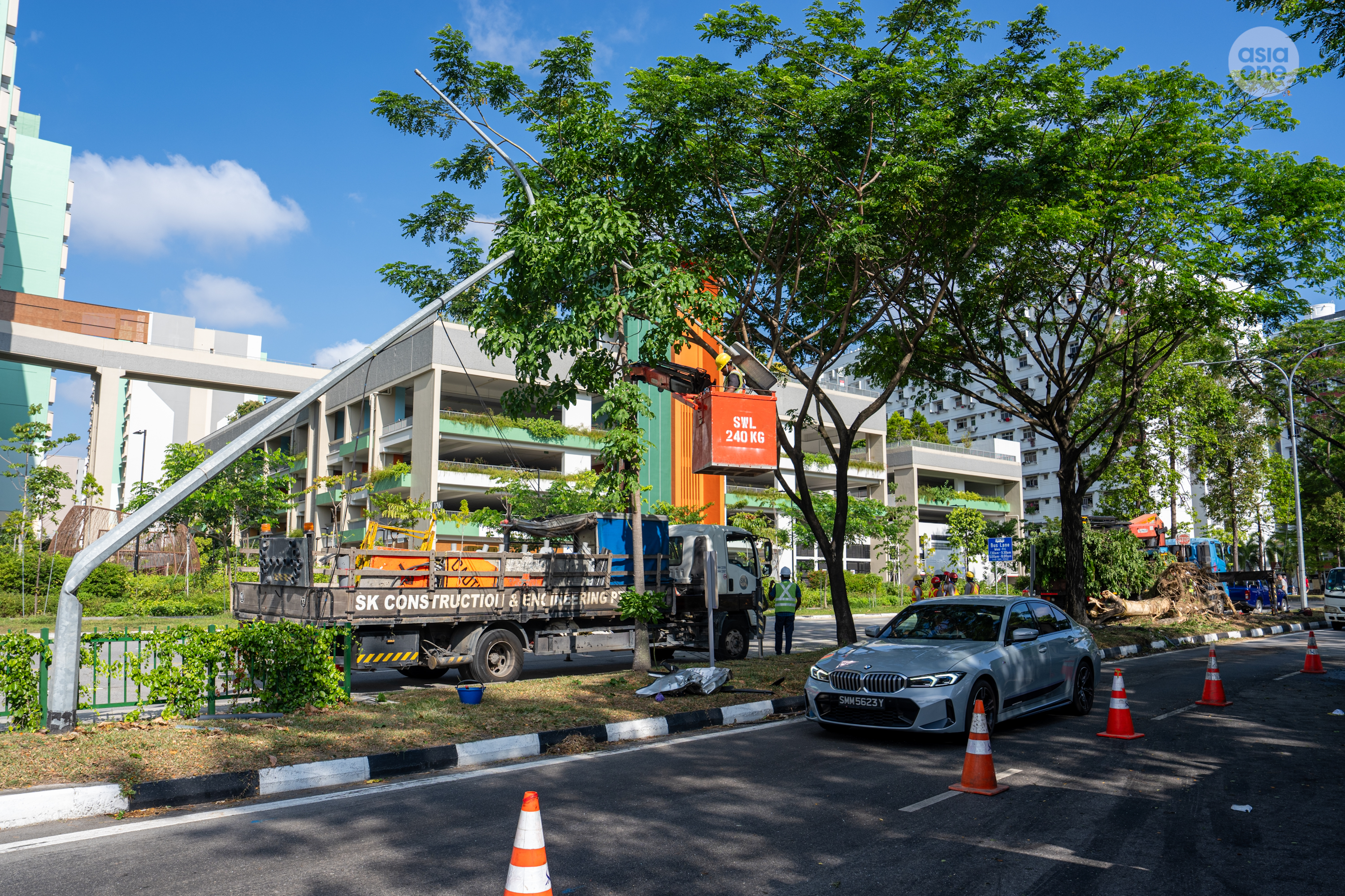 Construction workers removing a damaged lamp post. The fallen tree sits in the background.