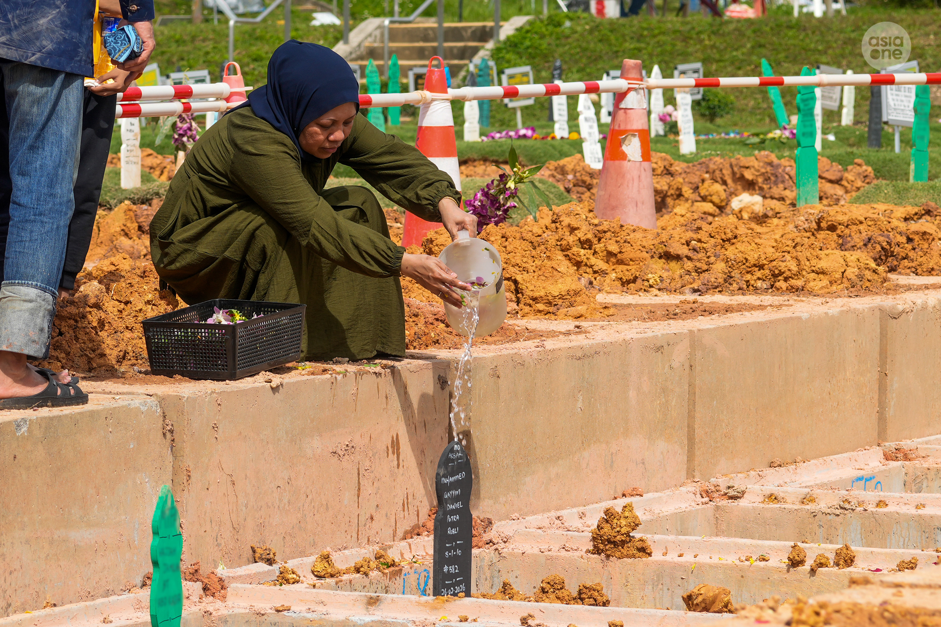 Madam Siti sprinkling water over Daniel's grave.